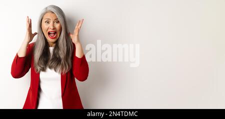 Asiatische Senior Geschäftsfrau schreien und schauen empört, fühlen sich beunruhigt und schreien, vor weißem Hintergrund stehen Stockfoto