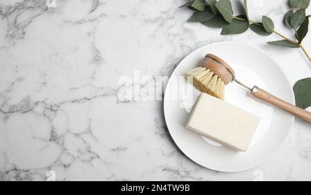 Reinigungsbürste, Seifenleiste und Teller auf weißem Marmortisch, flach liegend mit Platz für Text. Geschirrspülmittel Stockfoto