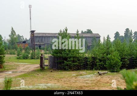 Verlassene, ausgebrannte Mitarbeiter des Unternehmens ein großer Holzhangar ist überwuchert mit jungen Kiefern am Ende der Straße im nördlichen Dorf Stockfoto