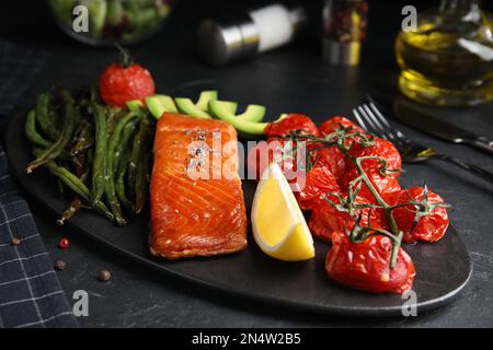 Leckerer gekochter Lachs und Gemüse auf schwarzem Tisch. Gesunde Mahlzeiten aus der Airfryer Stockfoto