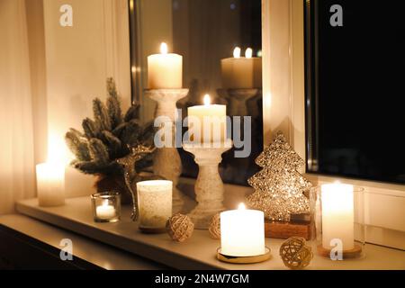 Brennende Kerzen und Weihnachtsdekor am Fensterbrett bei Nacht Stockfoto