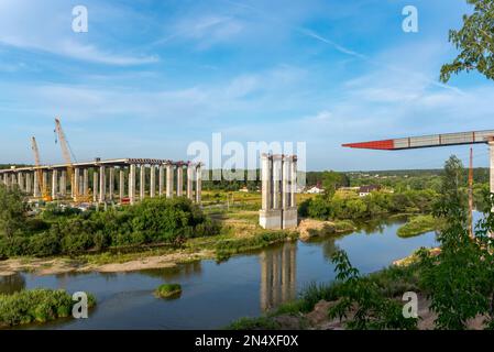 Bau einer Straßenbrücke über den Fluss. Verbindung von Spannen auf der Flusslinie beim Bau der nördlichen Umgehungsstraße im Sommer. Stockfoto