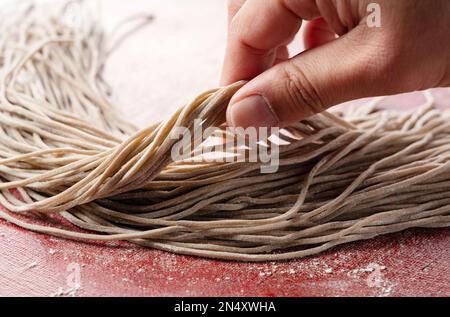 Eine Männerhand mit rohen Soba-Nudeln. Soba vor dem Kochen. Frisch zubereitete Soba-Nudeln. Stockfoto