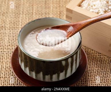 Amazake und ein Holzlöffel auf dem Tisch. Amazake ist ein traditionelles japanisches Süßgetränk. Stockfoto