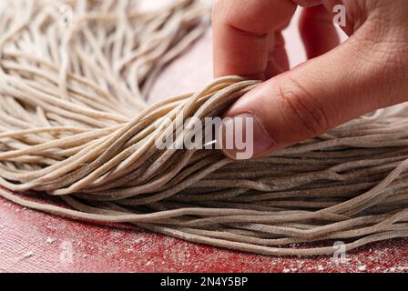 Eine Männerhand mit rohen Soba-Nudeln. Soba vor dem Kochen. Frisch zubereitete Soba-Nudeln. Stockfoto