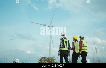 Rückansicht von drei Ingenieuren, die das Windturbinenfeld erörtern und deren Fortschritt prüfen. Stockfoto