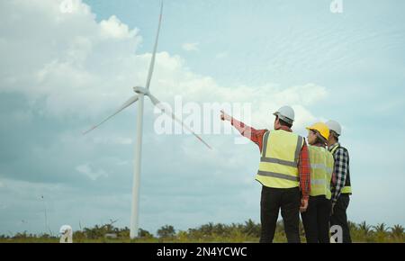 Rückansicht von drei Ingenieuren, die das Windturbinenfeld erörtern und deren Fortschritt prüfen. Stockfoto