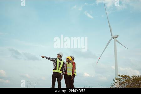 Rückansicht von drei Ingenieuren, die das Windturbinenfeld erörtern und deren Fortschritt prüfen. Stockfoto