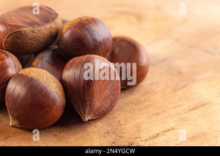 Ein Haufen rohe und ganze Kastanien auf einem Holztisch Stockfoto