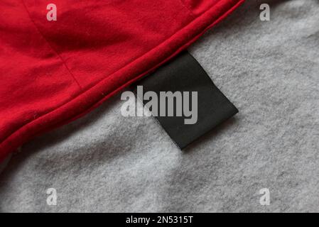 Leeres schwarzes Etikett für Wäschepflegesachen auf rot-grauen Textilhintergründen. Stockfoto