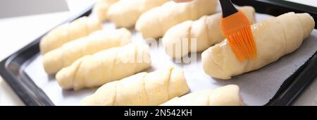 Der Koch bürstet rohe Croissants mit der Bürste im Eigelb-Kochvorgang Stockfoto