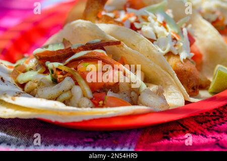 Mexikanische Baja Fisch-Tacos in Todos Santos mit frischer Sauce auf farbenfrohem Hintergrund. Tacos mit Jakobsmuscheln, Marlin, weißem Fisch und Garnelen mit Habanero Salsa Stockfoto