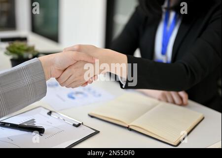 Nahaufnahme von zwei Geschäftsfrauen, die sich am Schreibtisch die Hand schütteln. Teamarbeit, Kollegen, Glückwunsch, Unterstützung, Begrüßung Stockfoto