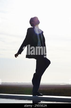 Der Himmel ist die Grenze. Silhouettenbild eines jungen Mannes im Anzug, der gegen den Morgenhimmel tanzt. Stockfoto