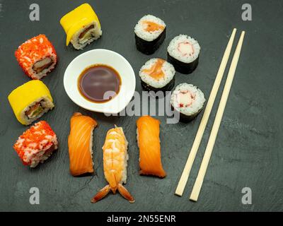 Von oben genießen Sie Sushi-Brötchen mit Garnelen und Lachs, serviert mit Sojasauce und Essstäbchen Stockfoto