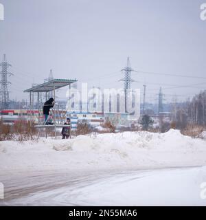 Ein Fotograf auf einem Hügel fotografiert die Straße neben einem lächelnden Mädchen im Winter von einem Stativ aus. Stockfoto