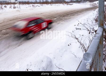 Eine kleine Glaskugel liegt im Winter leise auf dem Geländer im Schnee vor dem Hintergrund einer Kurve auf einer schlammigen Straße und der Silhouette einer Rennbahn Stockfoto