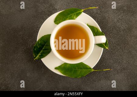 Teeblätter mit einer Tasse grünem Tee auf schwarzem Hintergrund Stockfoto