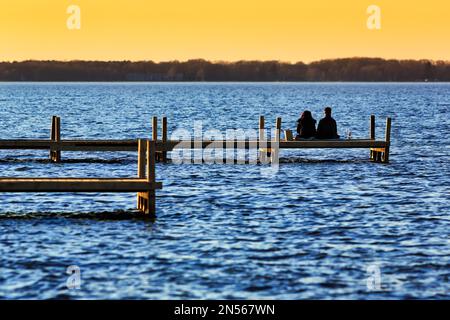 Ein Paar sitzt auf dem Steg und genießt den Sonnenuntergang im Steinhuder Meer, Steinhude, Niedersachsen, Deutschland Stockfoto