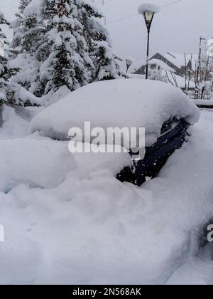 Blaues Auto unter einem Schneehaufen, geparkt auf der Straße in der Schneebank nach Schneesturm Stockfoto