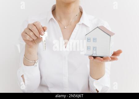 Frau mit Schlüssel, kleines Papierhaus, weißer Hintergrund. Auflösung und hochwertige Fotos Stockfoto