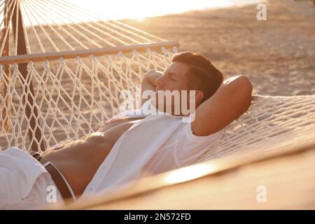 Ein Mann, der sich bei Sonnenuntergang in einer Hängematte am Strand entspannt Stockfoto