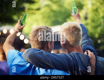 Ich liebe diese Band. Zwei gute Freunde trinken ihr Bier und grüßen von der guten Zeit auf einem Musikfestival. Stockfoto