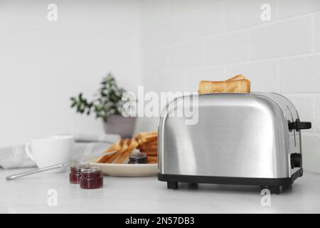 Moderner Toaster mit Brotscheiben und verschiedenen Marmeladen auf einem weißen Tisch in der Küche Stockfoto