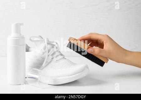 Frau putzt stilvolle Schuhe auf weißem Hintergrund, Nahaufnahme. Schuhpflegezubehör Stockfoto