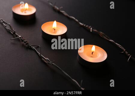 Brennende Kerzen und Stacheldraht auf schwarzem Hintergrund. Holocaust-Gedächtnisfeiertag Stockfoto