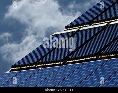 Auf dem Kombinationsdach wurden PV-Solarpaneele und die Solarwasserwärmeranlage auf braunem, geneigtem Lehmdach installiert. Sonnenkollektor Wasserleitungsheizungen Stockfoto