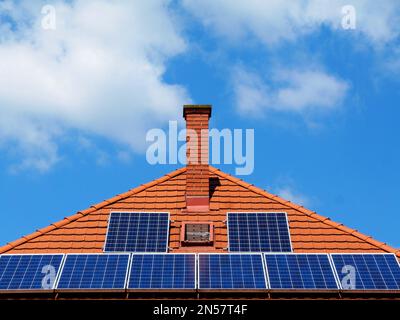 Solarpaneele für Photovoltaik-Sonnenkollektoren auf geneigtem Tonhausdach. Blauer Himmel und weiße Wolken. Alternative Energie. Umweltschutz. Außerhalb des Netzes Stockfoto