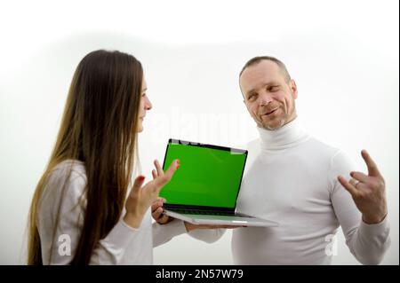 Mann und Mädchen in der Nähe eines Laptops mit grünem Bildschirm Chromakey gekleidet weißer Hintergrund der Mann erzählt der Lehrerin, dass sie sich neue Informationen anhört Online-Kommunikation Lerninteresse Unterhaltung Stockfoto