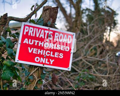 Ein deutliches Zeichen weißer Wörter auf rotem Hintergrund in einer Hecke weist darauf hin, dass die Straße vor Ihnen privat ist und nur zugelassene Fahrzeuge Zugang haben Stockfoto