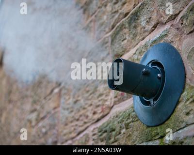 Wasserdampf aus dem Abzug eines Zentralheizungskessels kondensiert in kalter Luft. Der Schacht wird durch die Außenwand eines Sandsteingebäudes abgeleitet. Stockfoto