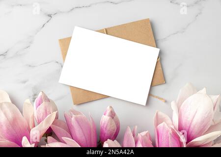 Leere Grußkarte oder Hochzeitseinladung mit pinkfarbenen Magnolienblumen auf weißem Marmorhintergrund. Modell. Flach verlegt Stockfoto