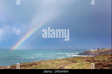 Ein heller Regenbogen erscheint auf dem Meer an einem sehr stürmischen Tag. Aus der Nähe der Levant Mine, mit Blick auf den Pendeen Lighthouse an der Küste von North Devon Stockfoto