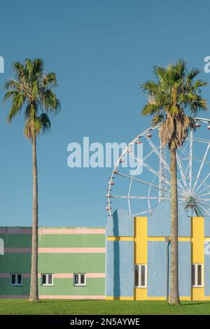 Die Fassade des Gebäudes ist in minimalen Pastelltönen gehalten und hat geometrische Linien mit Palmen und Riesenrad im Hintergrund. Abstrakte, farbenfrohe Architektur. Vertikal o Stockfoto