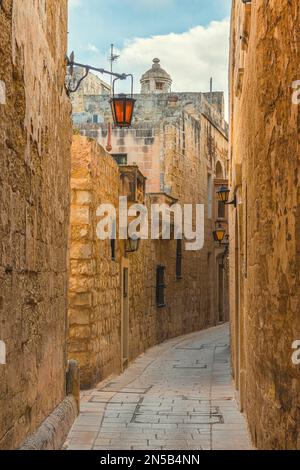 Alte mittelalterliche, enge Straße mit Straßenlaternen in Mdina, Malta mit niemandem. Vertikale Ausrichtung. Reiseziel Stockfoto