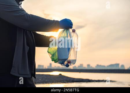 Der Mann hält Plastikflaschen in Mülltüten am Strand von Batumi City. Umweltverschmutzungskonzept. Ich sammle freiwillig Müll Stockfoto