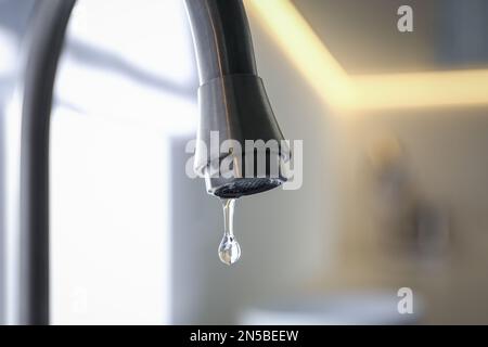 Wassertropfen fällt aus dem Wasserhahn auf verschwommenem Hintergrund, Nahaufnahme Stockfoto