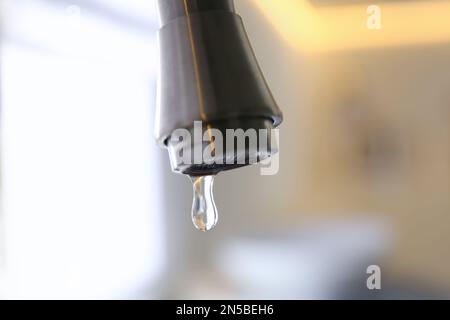 Wassertropfen fällt aus dem Wasserhahn auf verschwommenem Hintergrund, Nahaufnahme Stockfoto