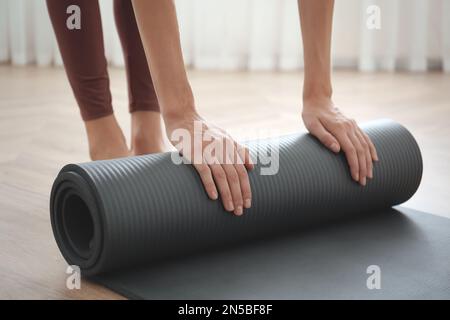 Frau rollt graue Yoga-Matte drinnen, Nahaufnahme Stockfoto