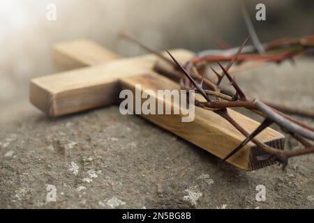 Dornenkrone und Holzkreuz auf Stein, Nahaufnahme. Ostereigenschaften Stockfoto