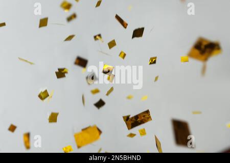 Glänzendes goldenes Konfetti, das auf hellgrauen Hintergrund herunterfällt Stockfoto