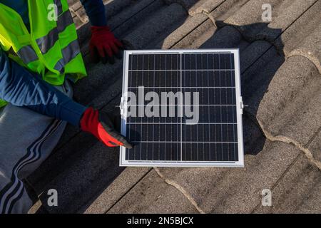 Ein Techniker installiert ein Solarpaneel auf einem Dach, nachhaltige Energie. Stockfoto