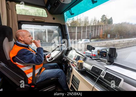 Professionelle Fernfahrer auf der Autobahn, frühstücken in der Fahrerkabine hinter dem Steuer Stockfoto