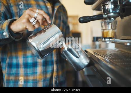 Barista im Coffee Shop, Hände des Mannes und Herstellung von Latte, Arbeit und Design mit Milchschaum und Espresso. Kleine Unternehmen, Verarbeitung und Ausgießen Stockfoto