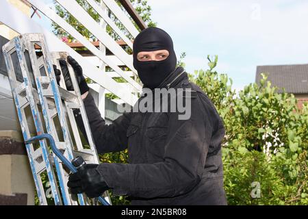 Einbrecher mit Brechstange und Taschenlampe auf einer Leiter auf einem Balkon Stockfoto