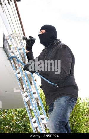 Einbrecher mit Brechstange und Taschenlampe auf einer Leiter auf einem Balkon Stockfoto